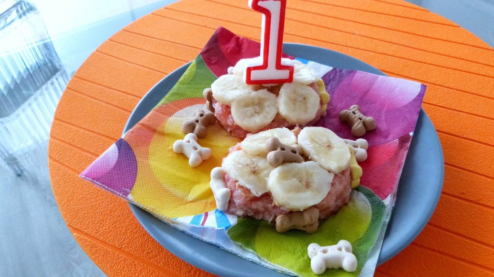 Torta de cumpleaños para perro con rodajas de banano, galletas con forma de hueso y una vela con el número uno, torta para perros